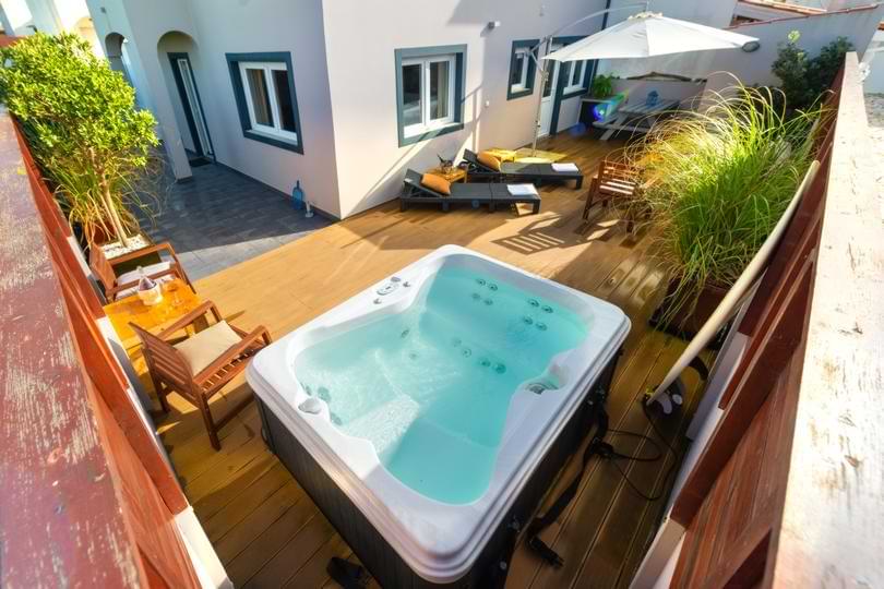 Private Outdoor Hot Tub Baleal Accommodation Aerial view of a private hot tub on a sunny wooden deck patio surrounded by lounge chairs and greenery.