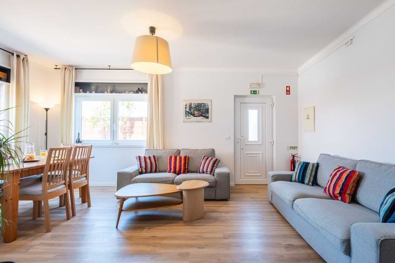 Baleal Holiday House Open Living Room Open-plan living room with comfortable grey sofas, wooden coffee tables, and a dining setup at Surf Atlantic holiday house.