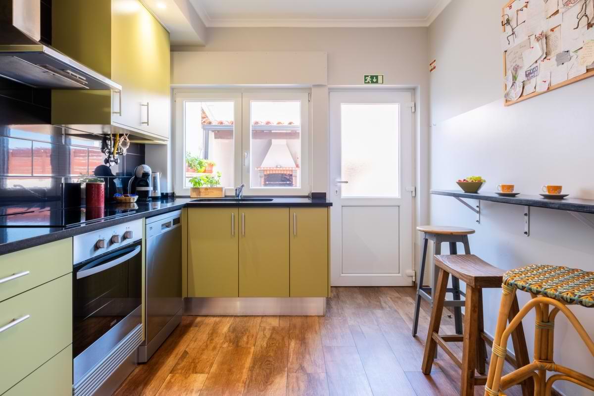 Fully Equipped Shared Kitchen – Surf Atlantic Modern self-catering kitchen at Surf Atlantic with green cabinets, breakfast bar with wooden stools, stove, and dishwasher.