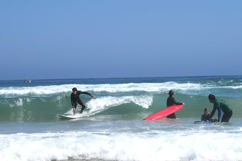 eginner Surf Coaching in the Ocean with Surf Atlantic A surf instructor guiding a beginner student catching a wave in gentle ocean waters during a private surf coaching session in Baleal.