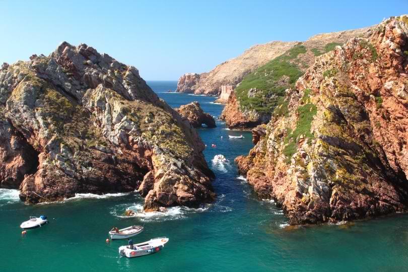 Small boats anchored in turquoise waters near the dramatic granite cliffs of Berlenga Island near Peniche, Portugal