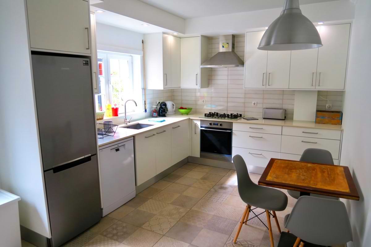 Bright, fully equipped white kitchen featuring a stainless steel refrigerator, oven, dishwasher, and a small dining table at Chillax Villa.