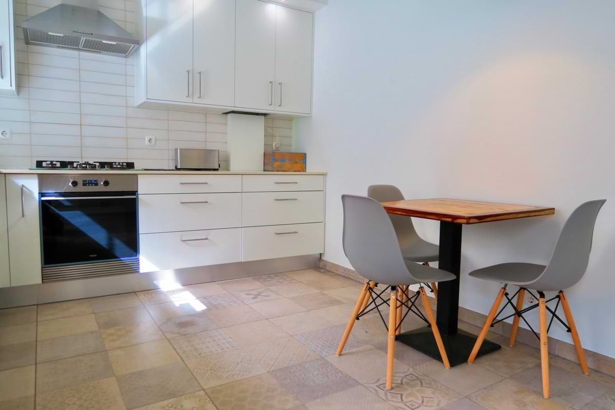 Close-up of the wooden breakfast table and grey chairs next to the built-in oven and white cabinets in the Chillax Villa kitchen.