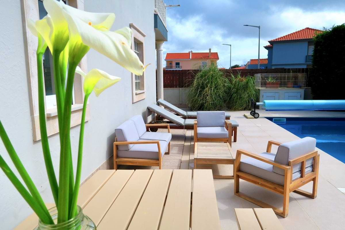 Wooden outdoor lounge furniture and dining table with fresh calla lilies next to the swimming pool at Chillax Villa.