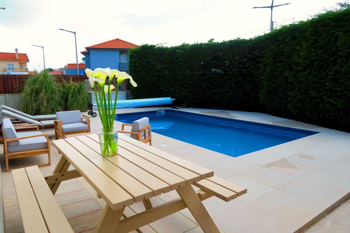 Wooden picnic dining table with white flowers in a vase sitting next to the private swimming pool at Chillax Villa rental.