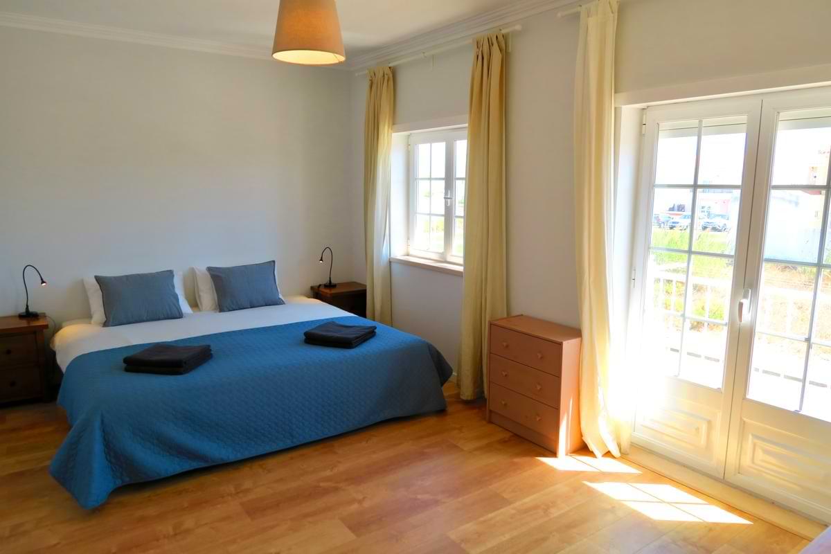 Large double bedroom with blue runner, nightstands, and glass doors opening to outdoor natural light at Chillax Villa.