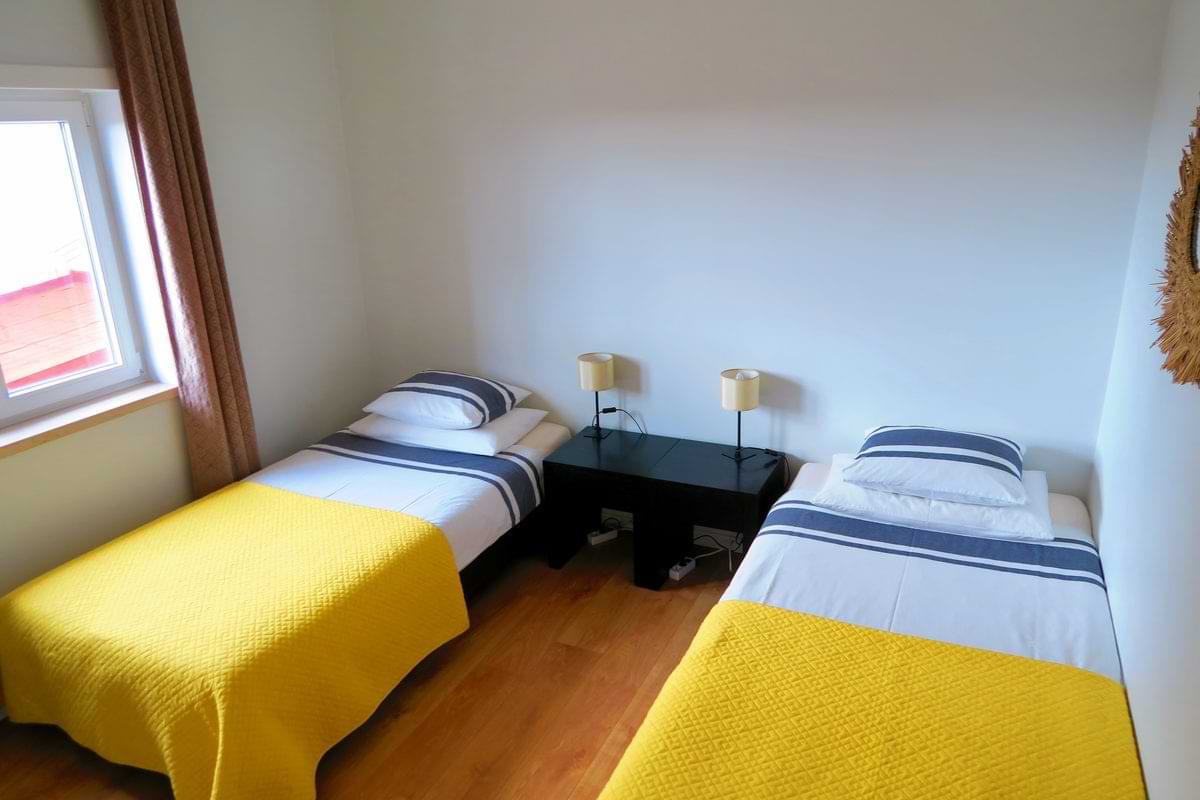Twin bedroom at Chillax Villa set up with two single beds featuring bright yellow blankets and striped pillows next to a dark nightstand. 