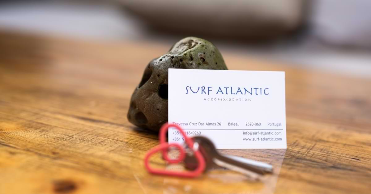 Close-up of a Surf Atlantic Accommodation business card and keys on a rustic wooden desk