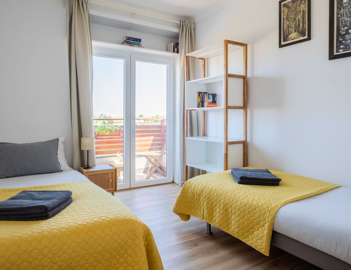 Bright bedroom with twin beds, bookshelf and balcony access