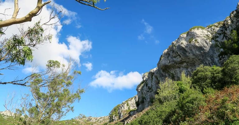 Scenic view of the limestone rock climbing crags and green hills of Serra de Montejunto, Portugal under a bright blue sky.