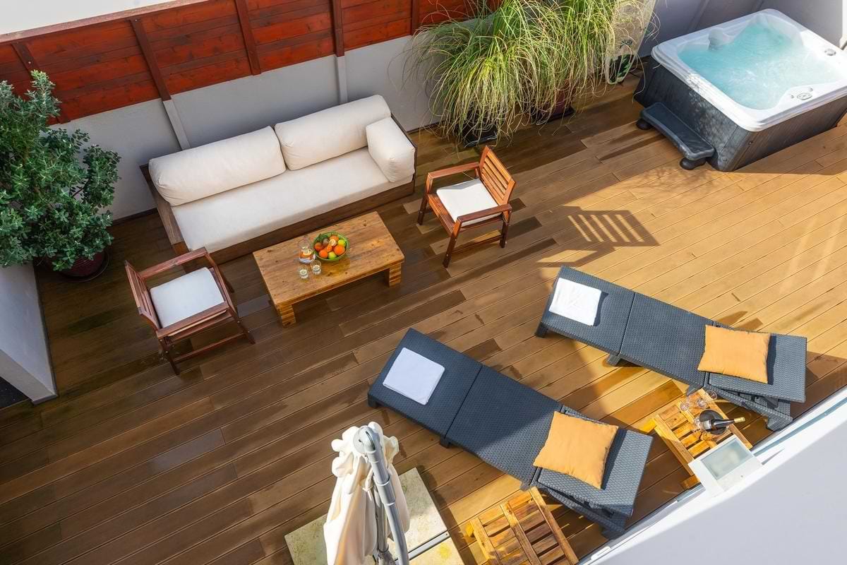 Overhead view of the entire wooden patio deck featuring a white outdoor sofa, coffee table with fruit, dark sun loungers, and the hot tub corner.