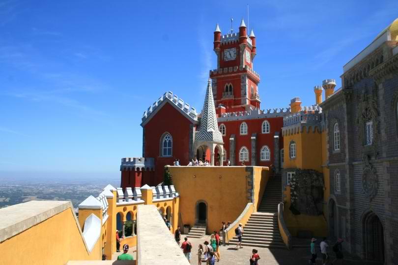 Vibrant yellow and red towers of Pena Palace set against lush green hills in Sintra, Portugal