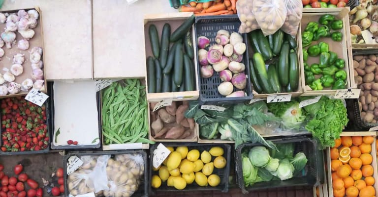 Overhead view of crates filled with fresh vegetables, garlic, potatoes, and fruit at Peniche Food Market in Portugal.