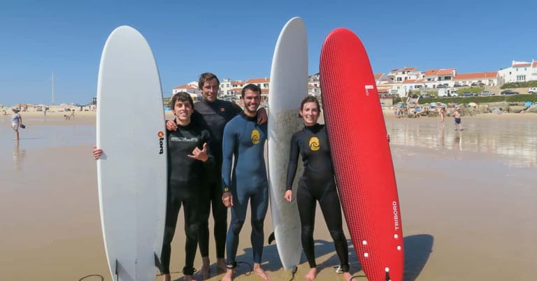 A small group of smiling surfers in wetsuits holding surfboards on the beach during a private surf lesson with Surf Atlantic in Baleal, Peniche.