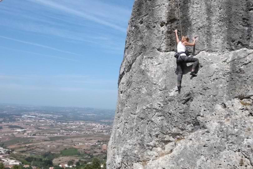 Climber Ascending Sport Route in Serra de Montejunto A climber scaling a vertical limestone rock face on a sport climbing route overlooking the Montejunto valley in Portugal.