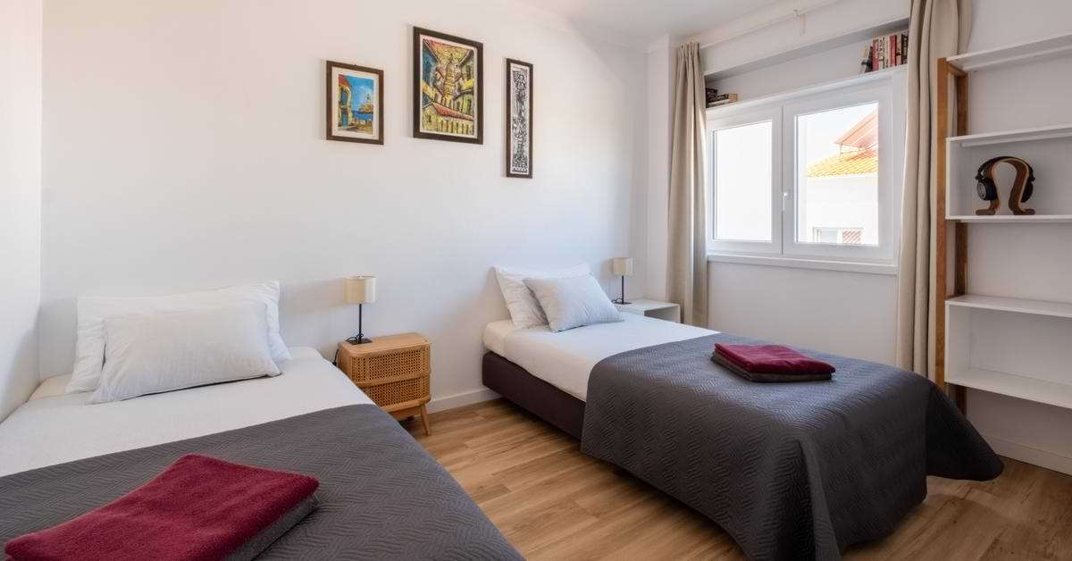 Bright twin bedroom with white linens, wooden nightstands, and framed wall art at Surf Atlantic in Baleal.