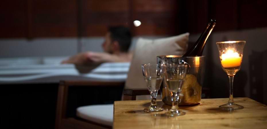 Relaxing Evening Spa Experience Candlelit hot tub setup with wine glass and champagne bucket on a wooden table at night.