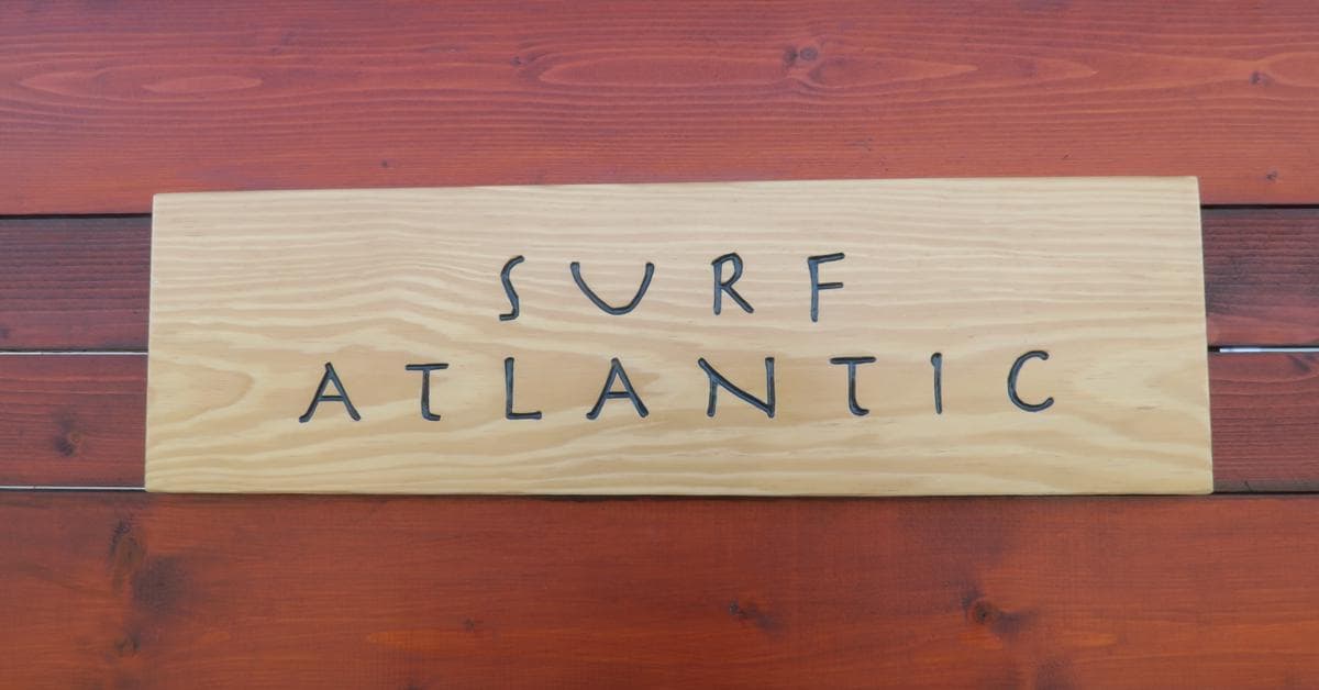 A wooden sign reading "Surf Atlantic" mounted on a dark wood panel background for the Surf Atlantic Peniche blog.
