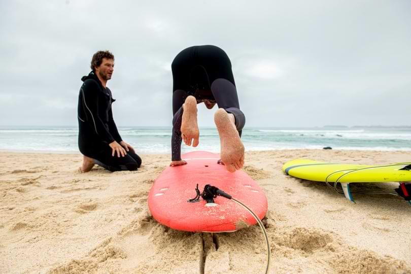 Tailored Surf Lessons on Baleal Beach Surf instructor guiding a student practicing pop-up mechanics on a soft-top surfboard on the beach in Baleal.